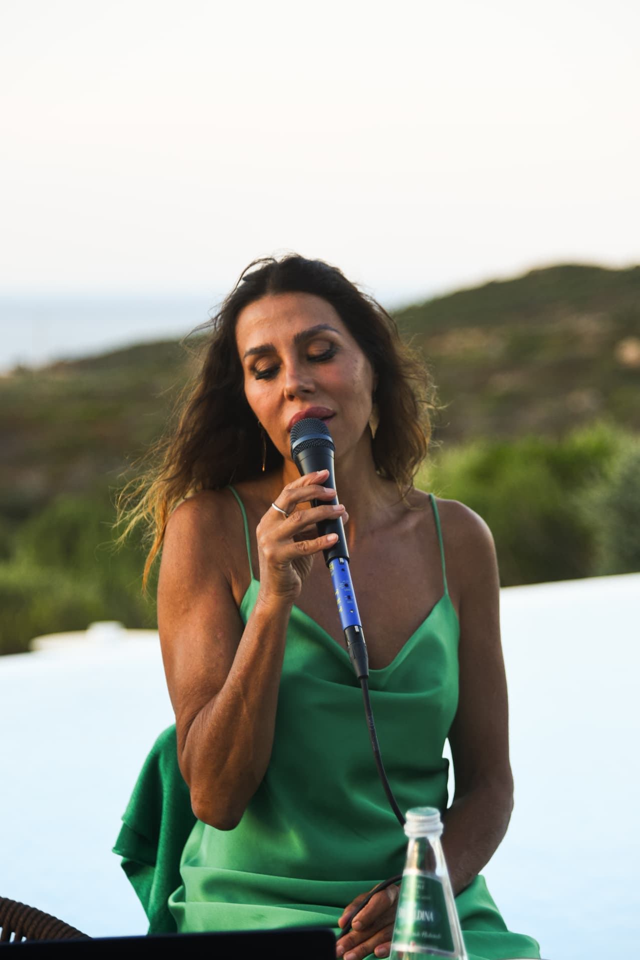 Cantante in abito verde si esibisce dal vivo con le colline della Gallura sullo sfondo