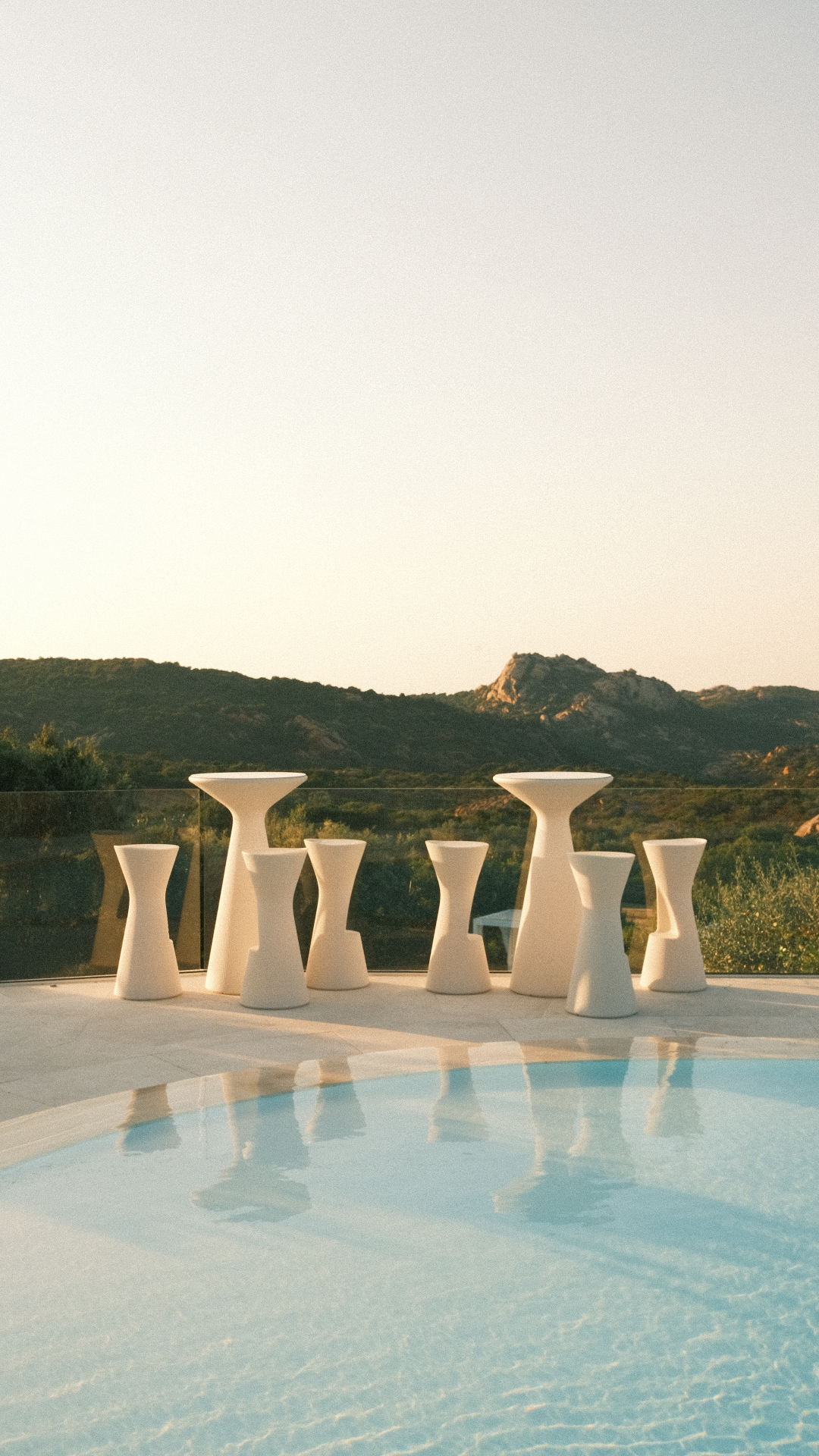 Tavoli alti in ceramica bianca accanto alla piscina al tramonto